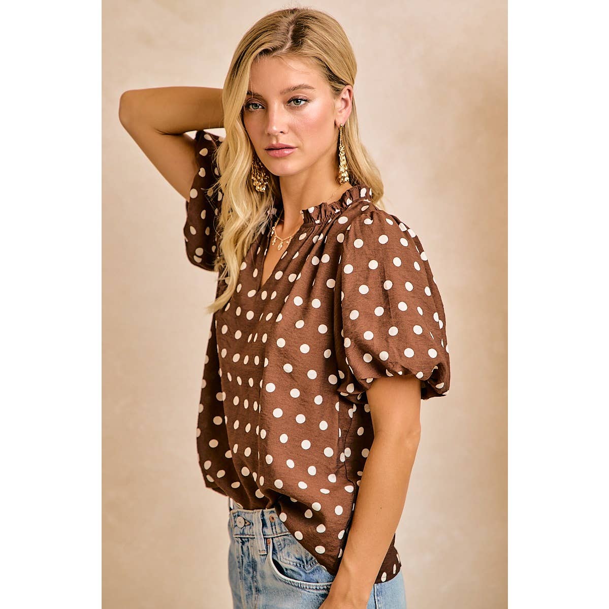 Woman wearing a brown polka dot blouse against a beige background