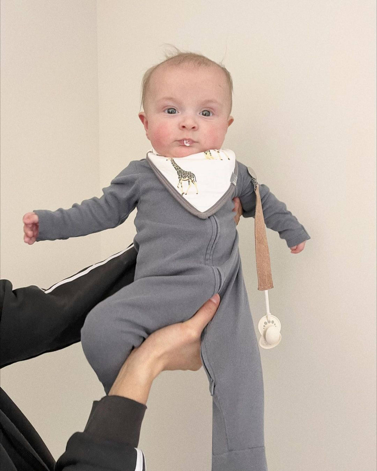 Baby holding pacifier with linen clip attached to outfit