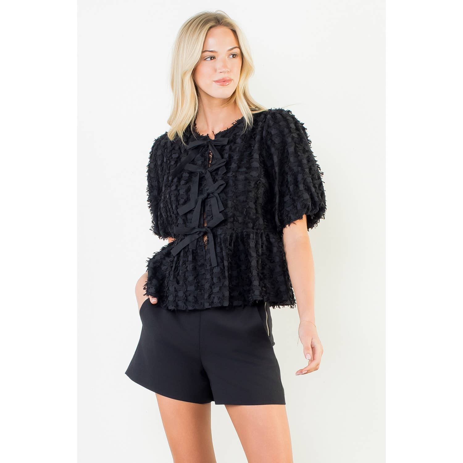 Woman wearing a black textured top and shorts on a white background