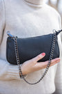 Black handbag with a chain strap held by a person wearing a beige sweater.