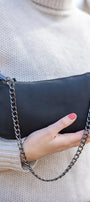 Black handbag with a chain strap held by a person wearing a beige sweater.