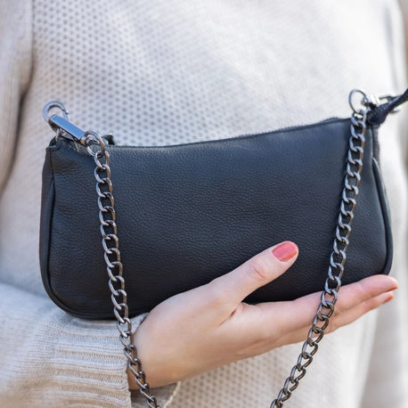 Black handbag with a chain strap held by a person wearing a beige sweater.