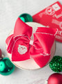 Red hair bow with a Santa Claus patch on a white surface with Christmas decorations.