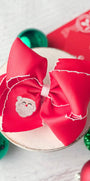 Red hair bow with a Santa Claus patch on a white surface with Christmas decorations.