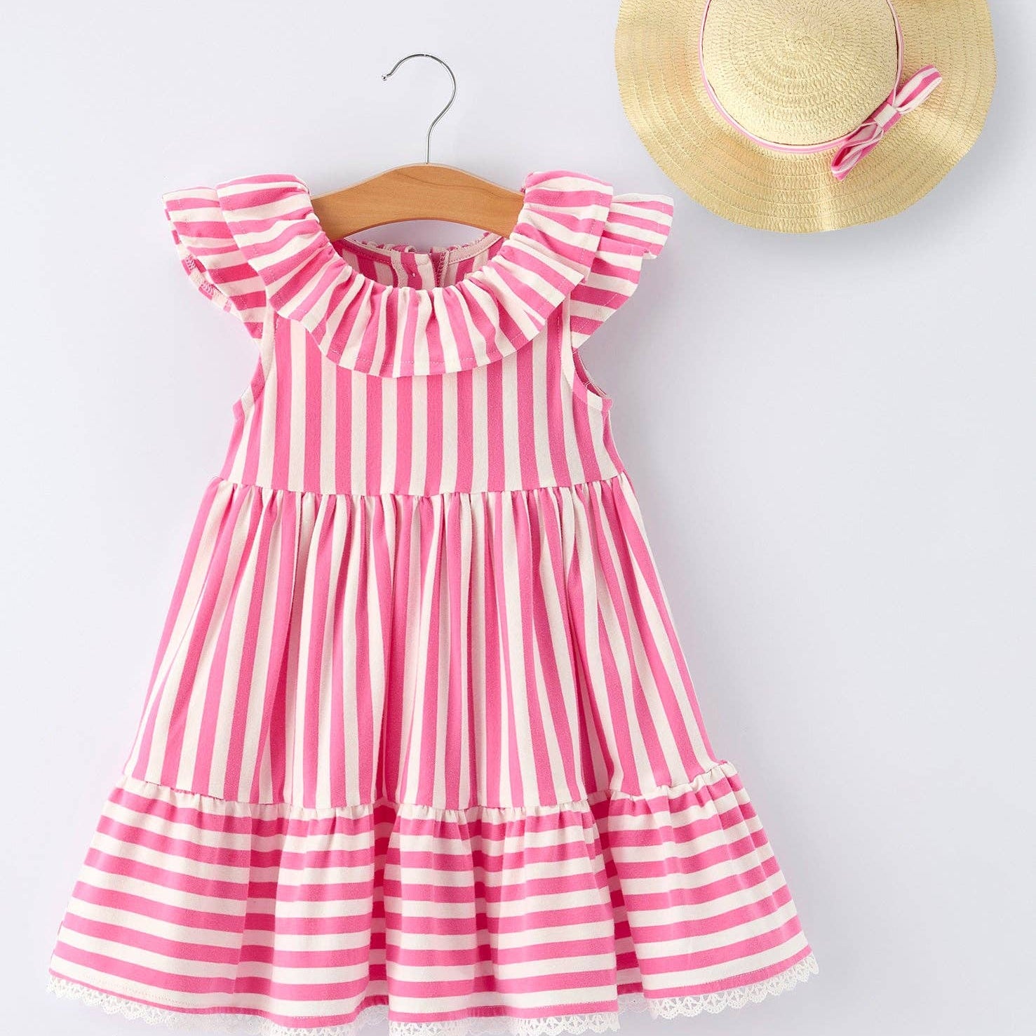 Pink and white striped dress on a hanger with a straw hat on a light gray background