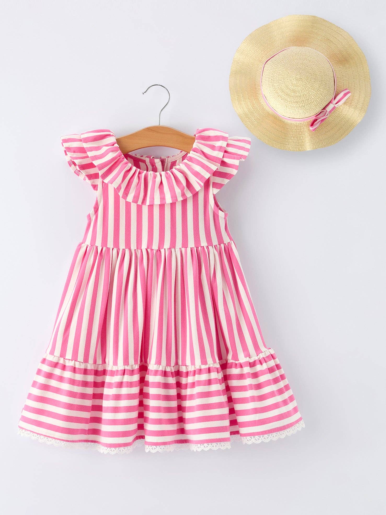 Pink and white striped dress on a hanger with a straw hat on a light gray background