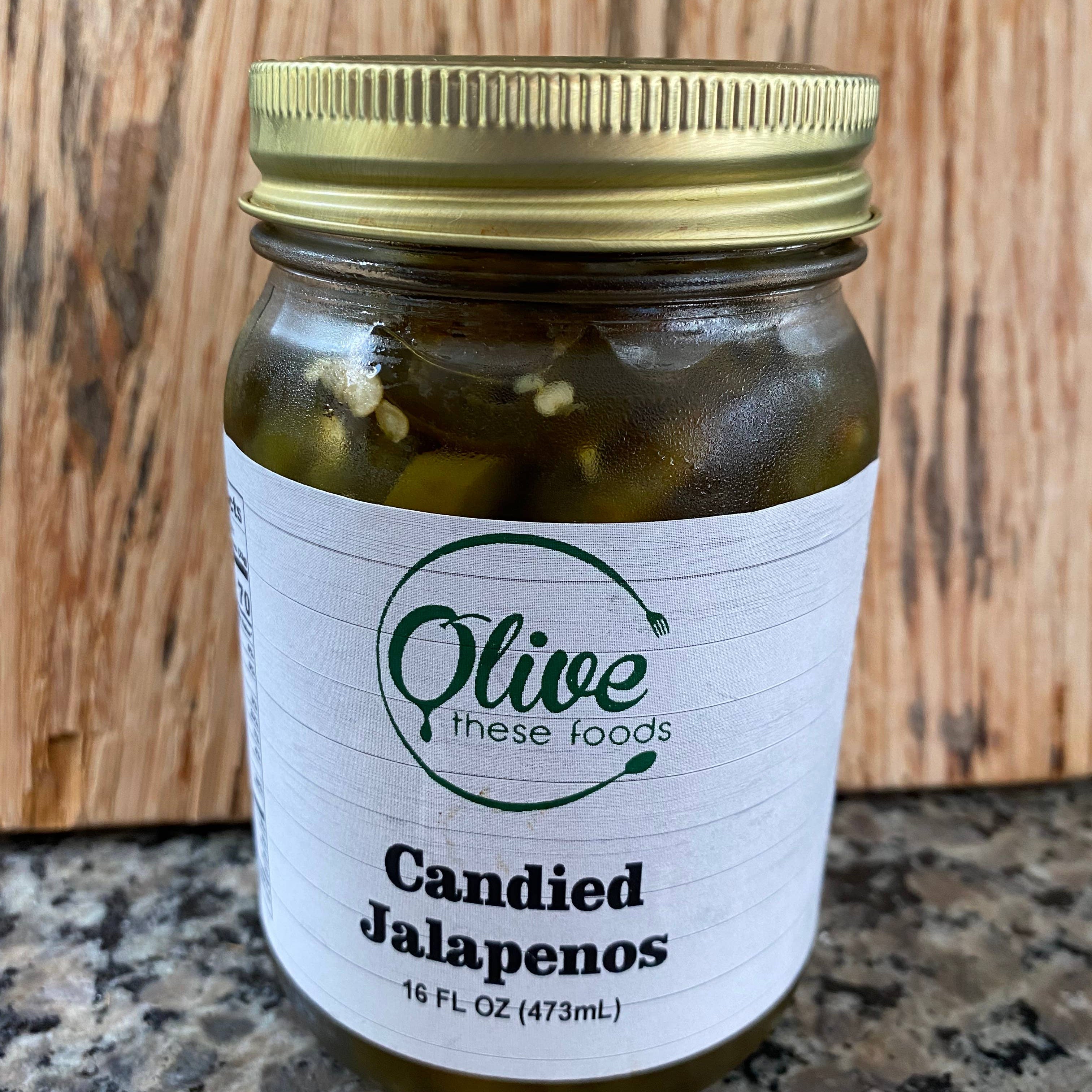 Jar of candied jalapenos with a gold lid on a wooden surface