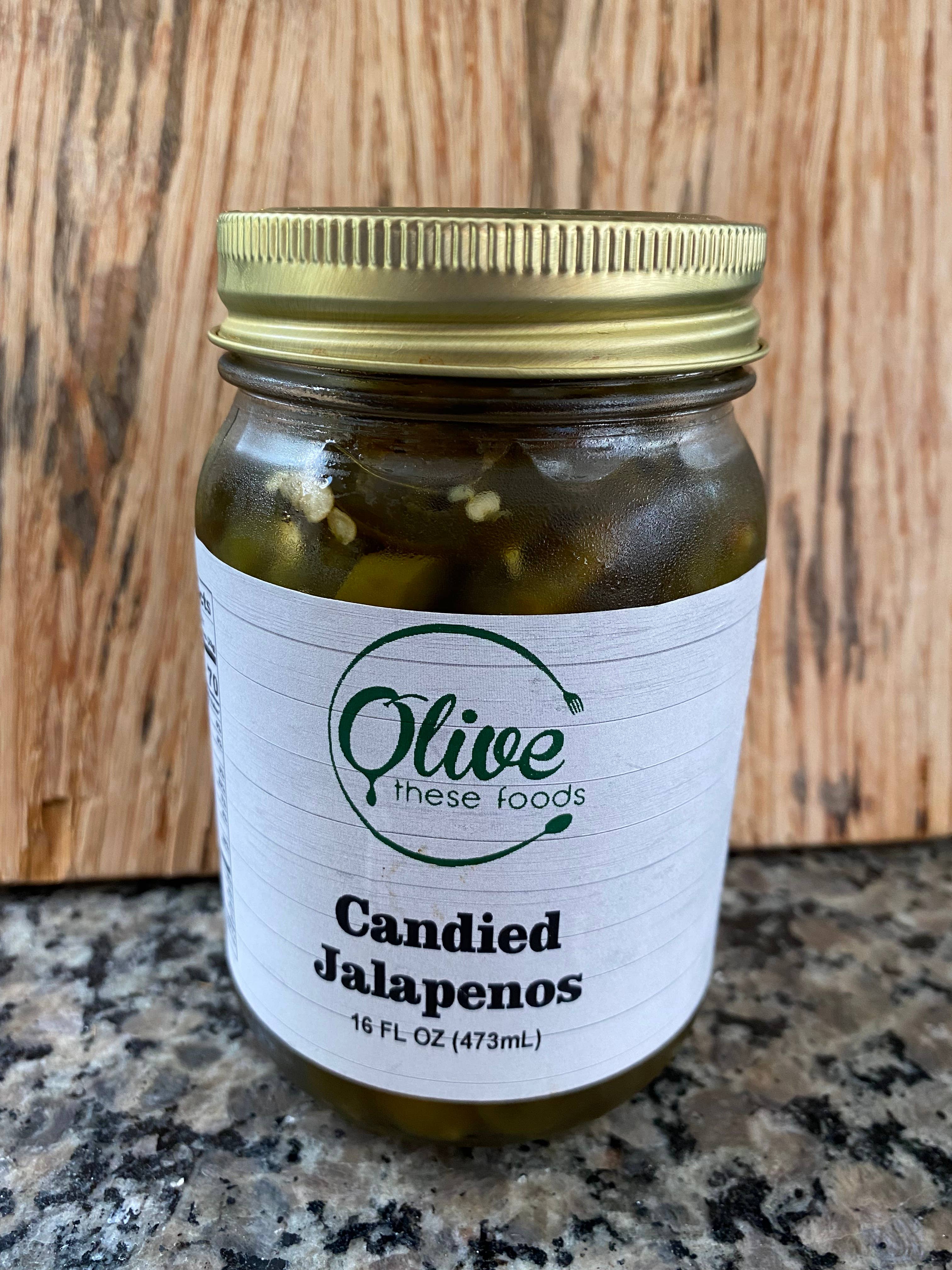 Jar of candied jalapenos with a gold lid on a wooden surface