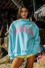 Person wearing a light blue sweatshirt with 'LOLLY GAG' text in pink, standing in a rustic outdoor setting.