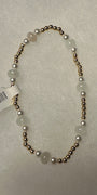 A beaded necklace with round white pearls and pale green stone beads separated by small metallic gold spacer beads, shown on a textured light gray background with a white product tag attached.