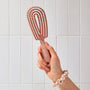 Hand holding a pink hairbrush against a tiled bathroom wall