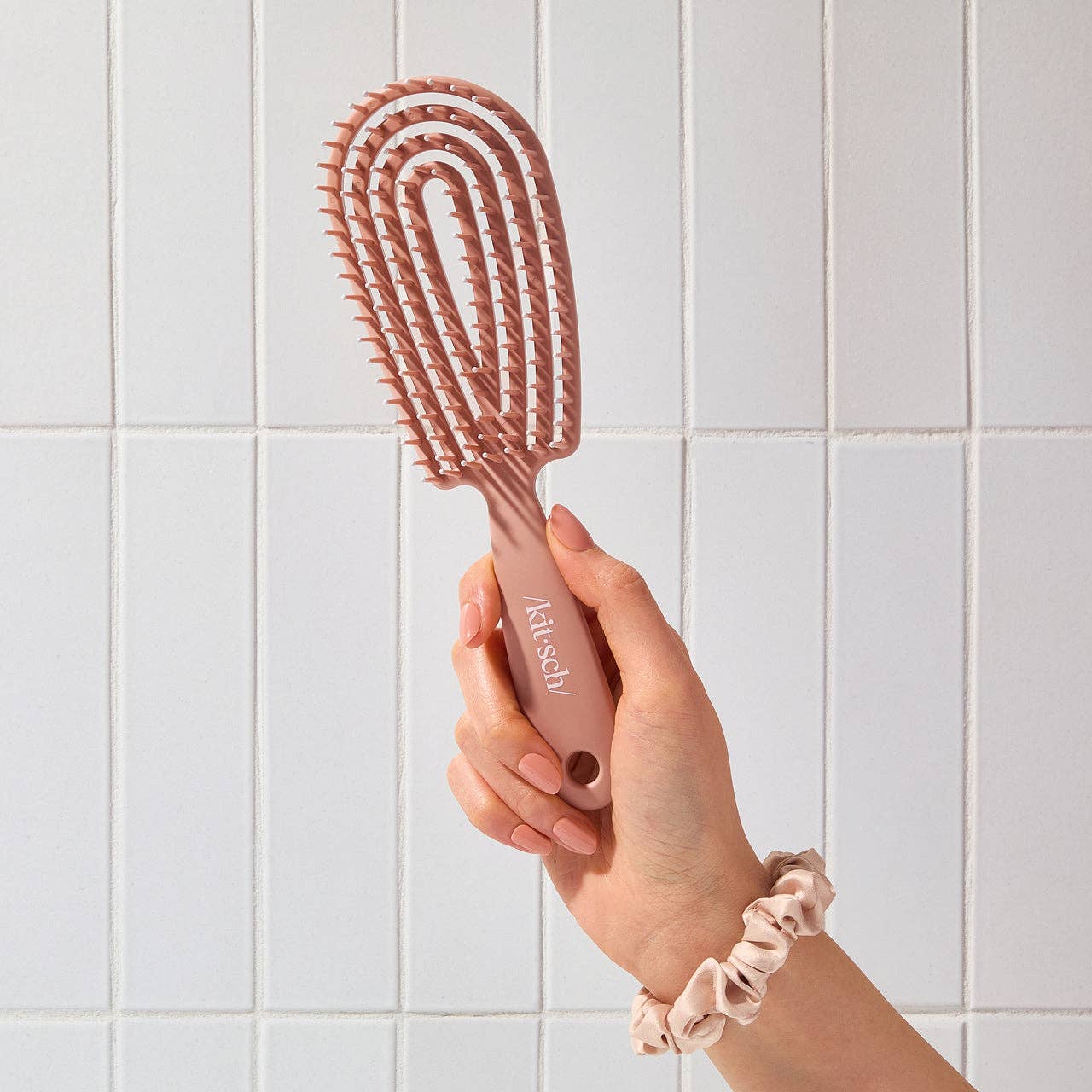 Hand holding a pink hairbrush against a tiled bathroom wall
