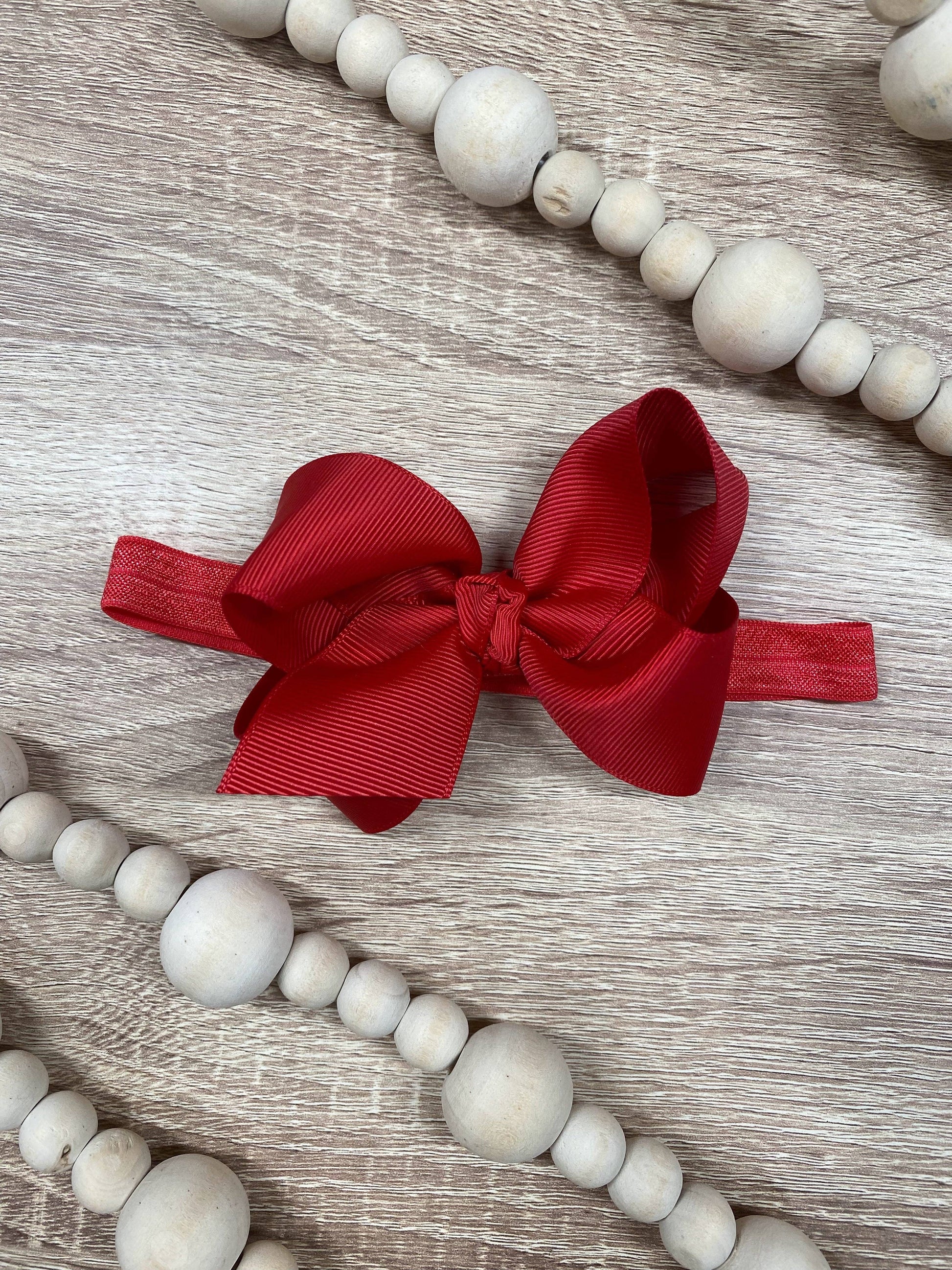 Red bow headband on a wooden surface with white beads