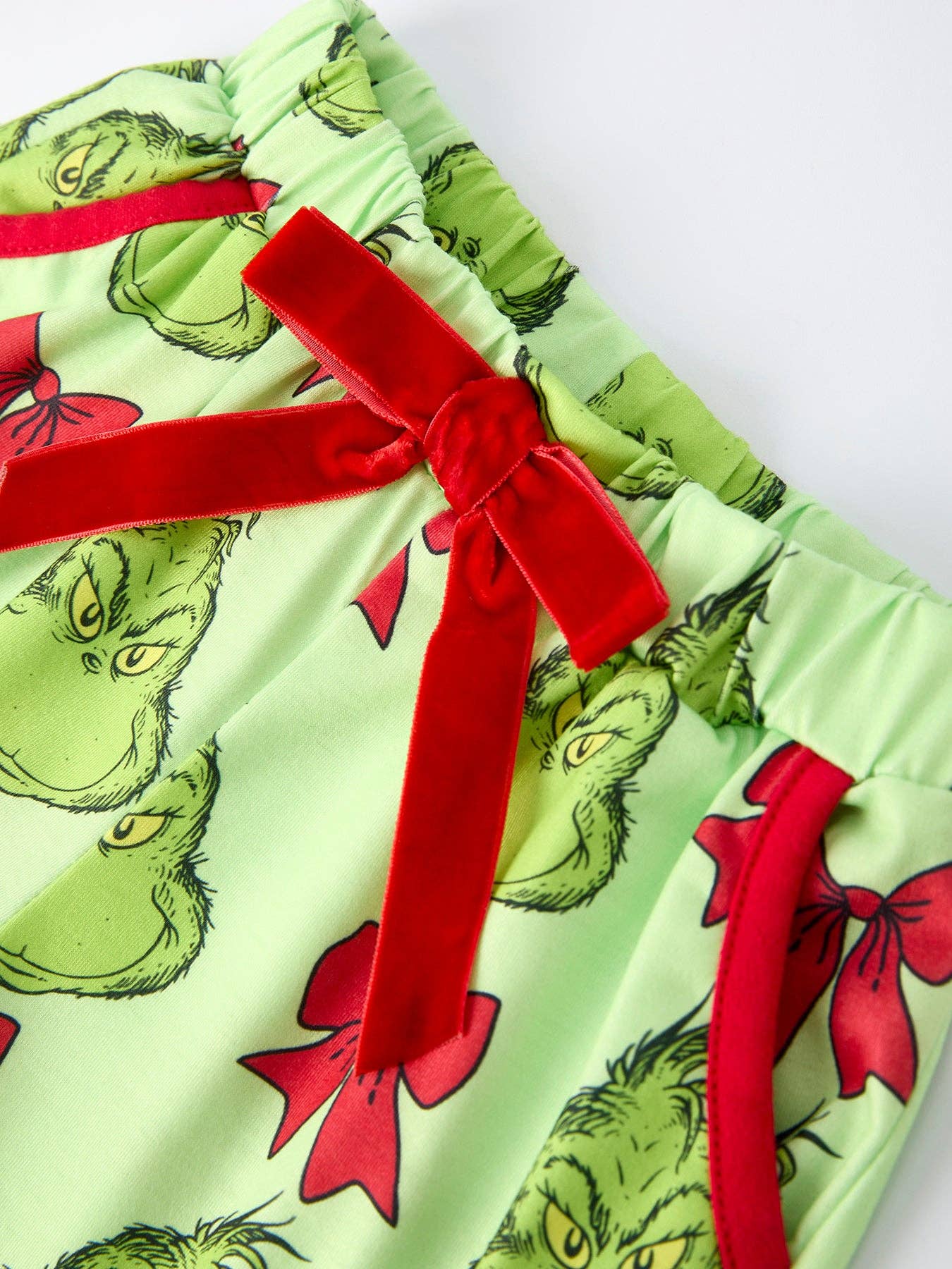 Green fabric with Grinch print and red bows on a white background