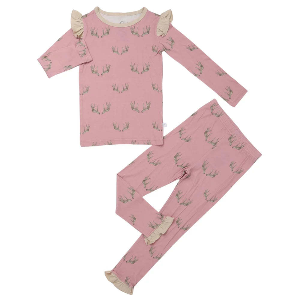 A two-piece children's pajama set in dusty pink, featuring an all-over green leaf pattern and beige ruffle trim on the collar and cuffs, laid flat on a white background.