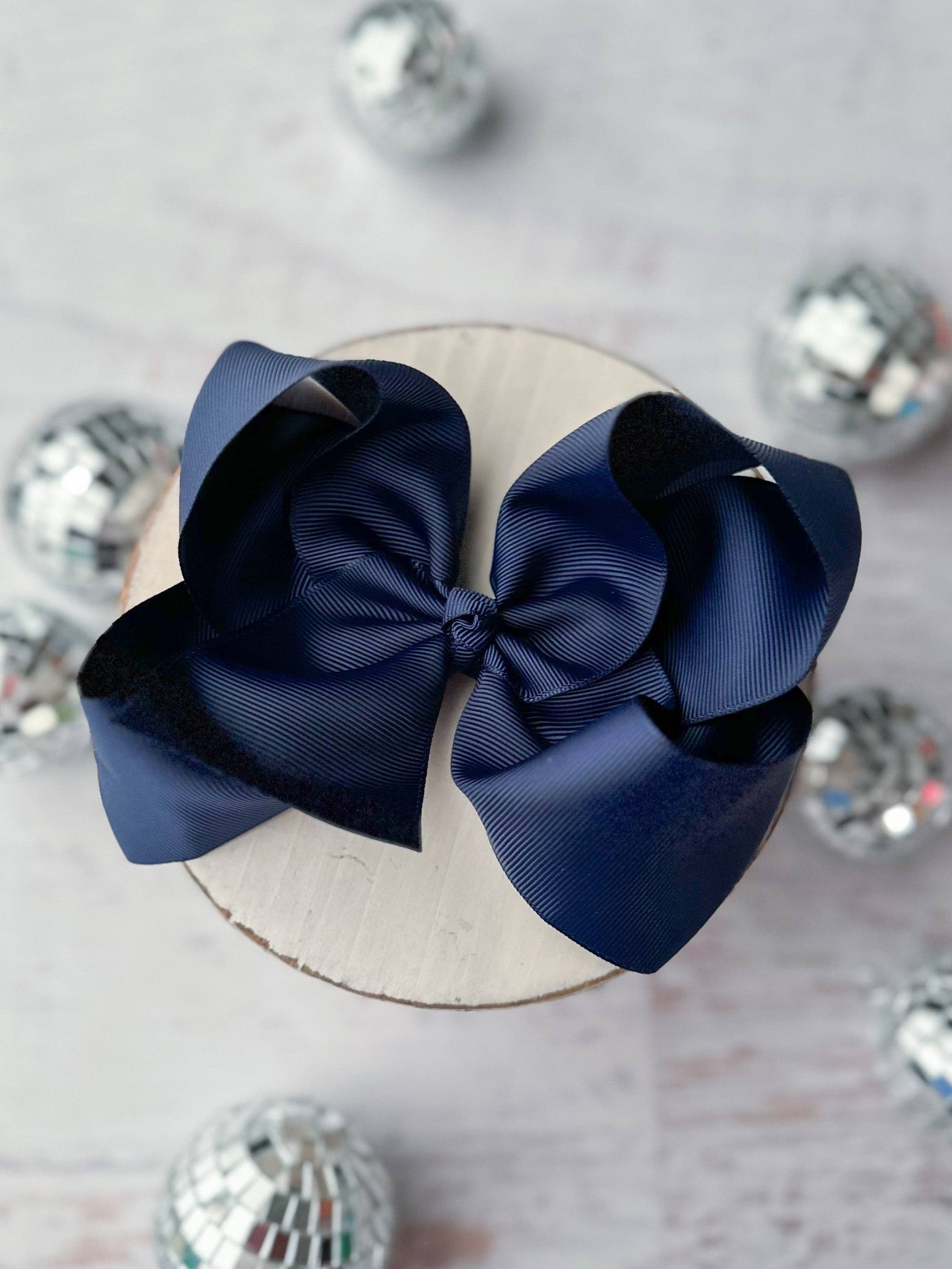 Navy blue hair bow on a white surface with decorative silver balls.