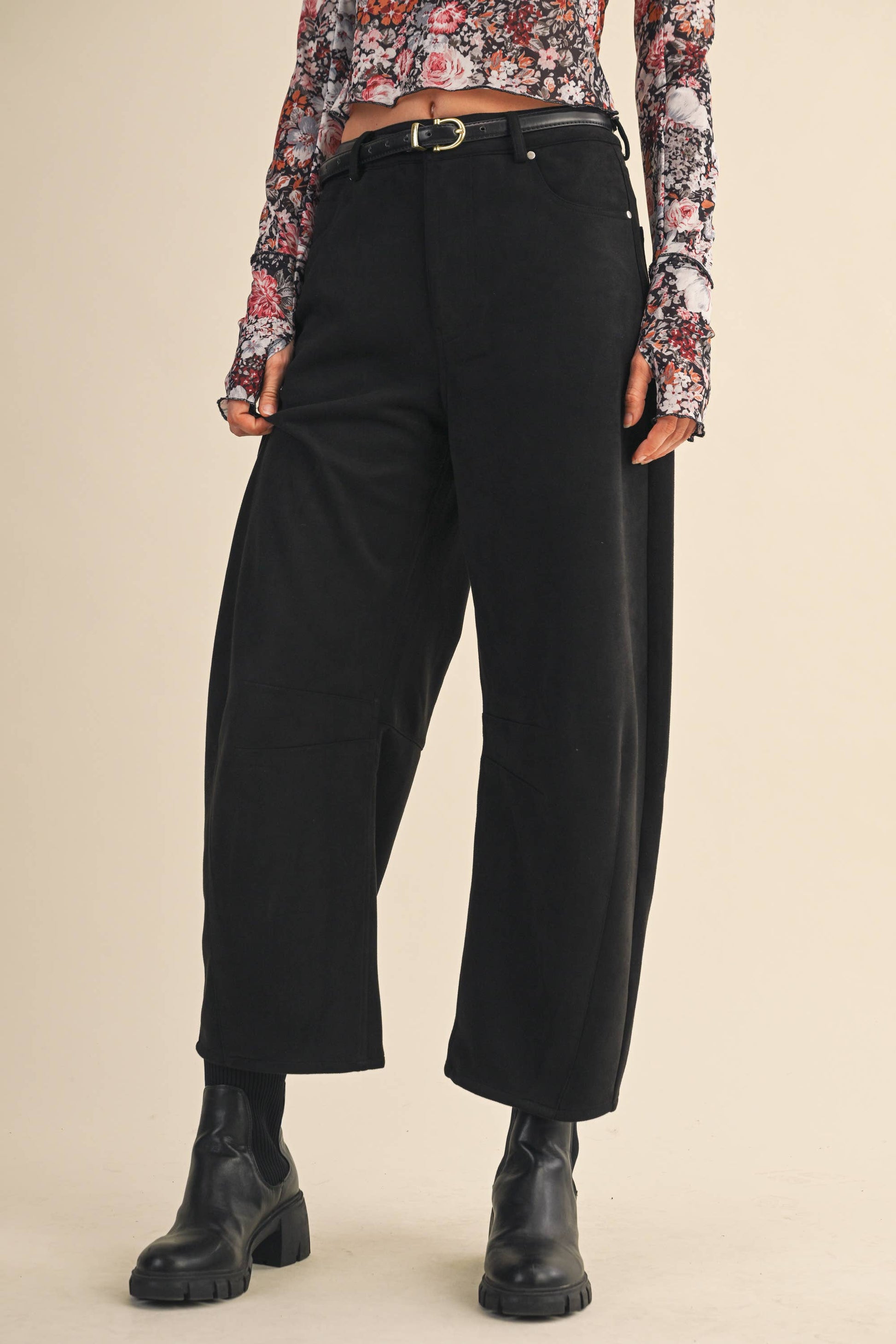 Person wearing black pants and a floral top on a beige background