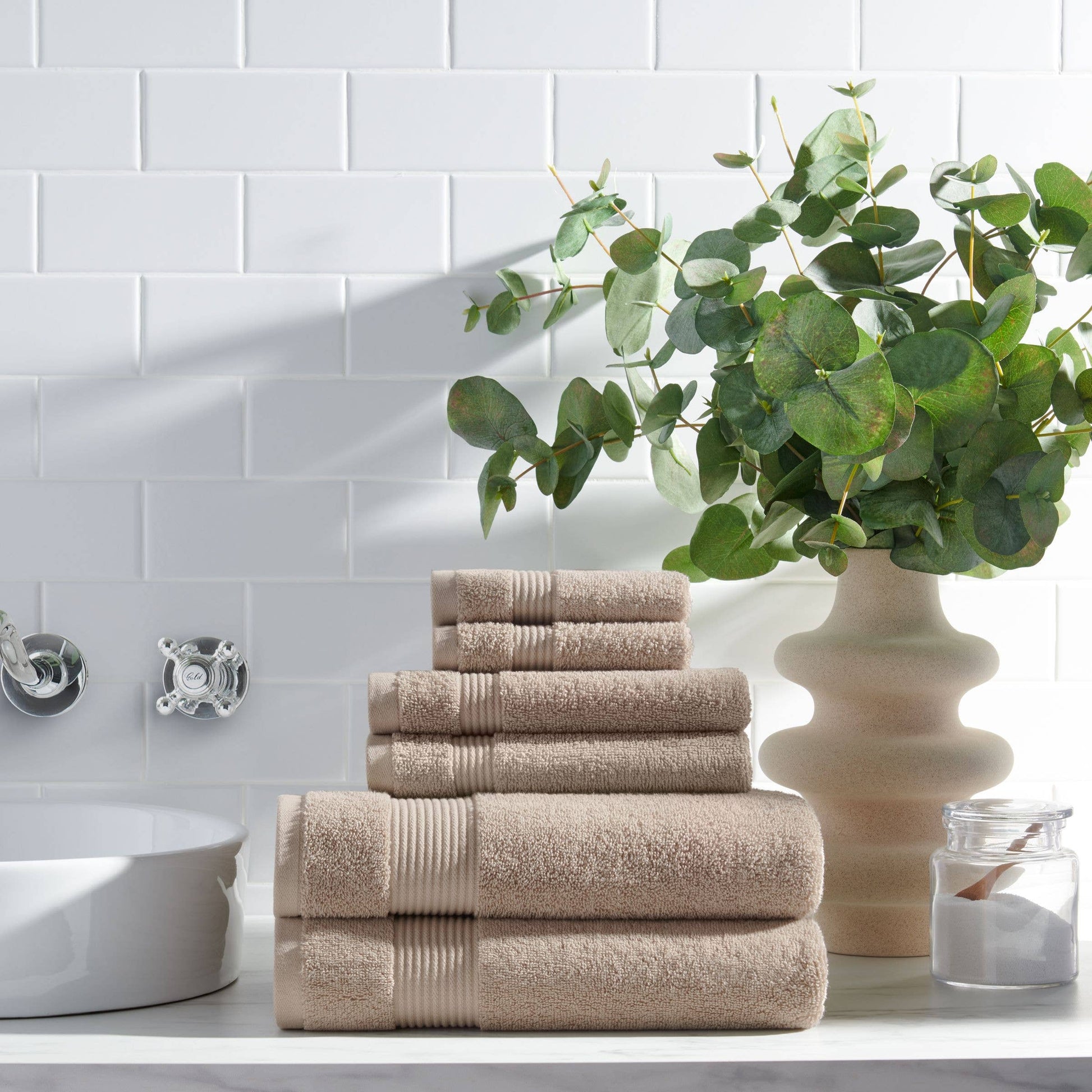 Stack of beige towels on a bathroom counter with a plant and decorative items.
