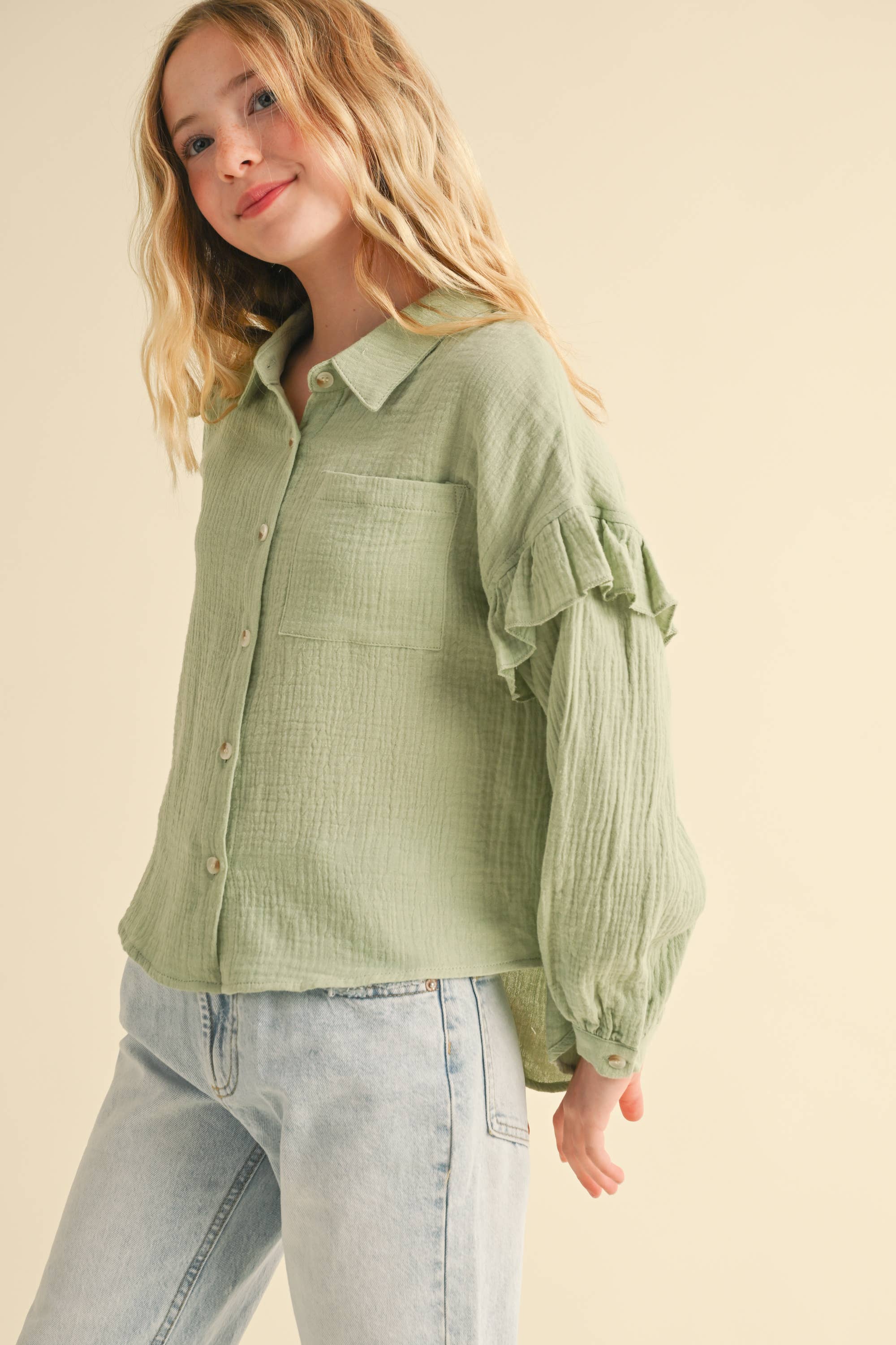 Woman wearing a green long sleeve shirt with a ruffle sleeves detail against a beige background