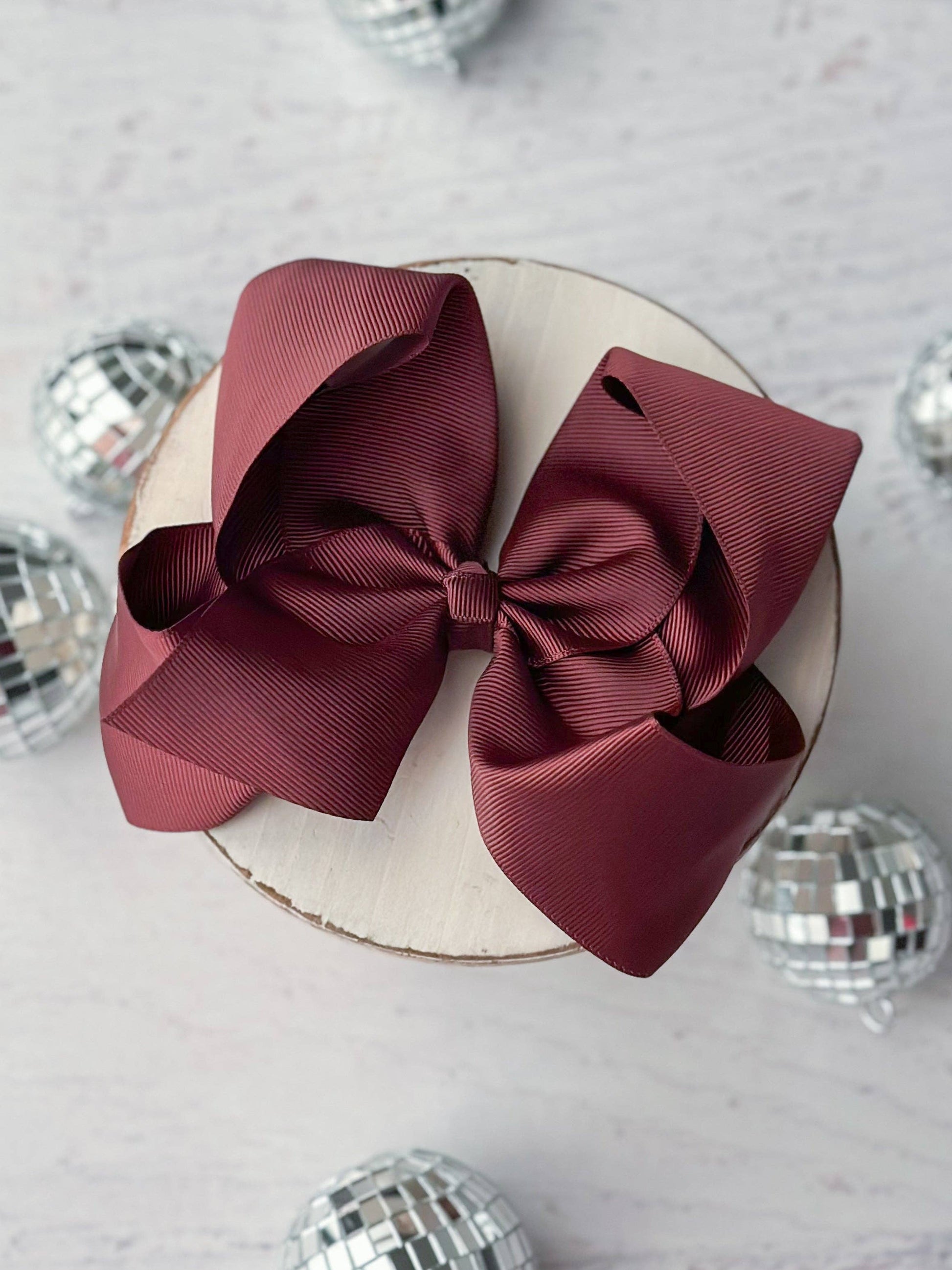 Large burgundy bow on a white cake with disco balls in the background