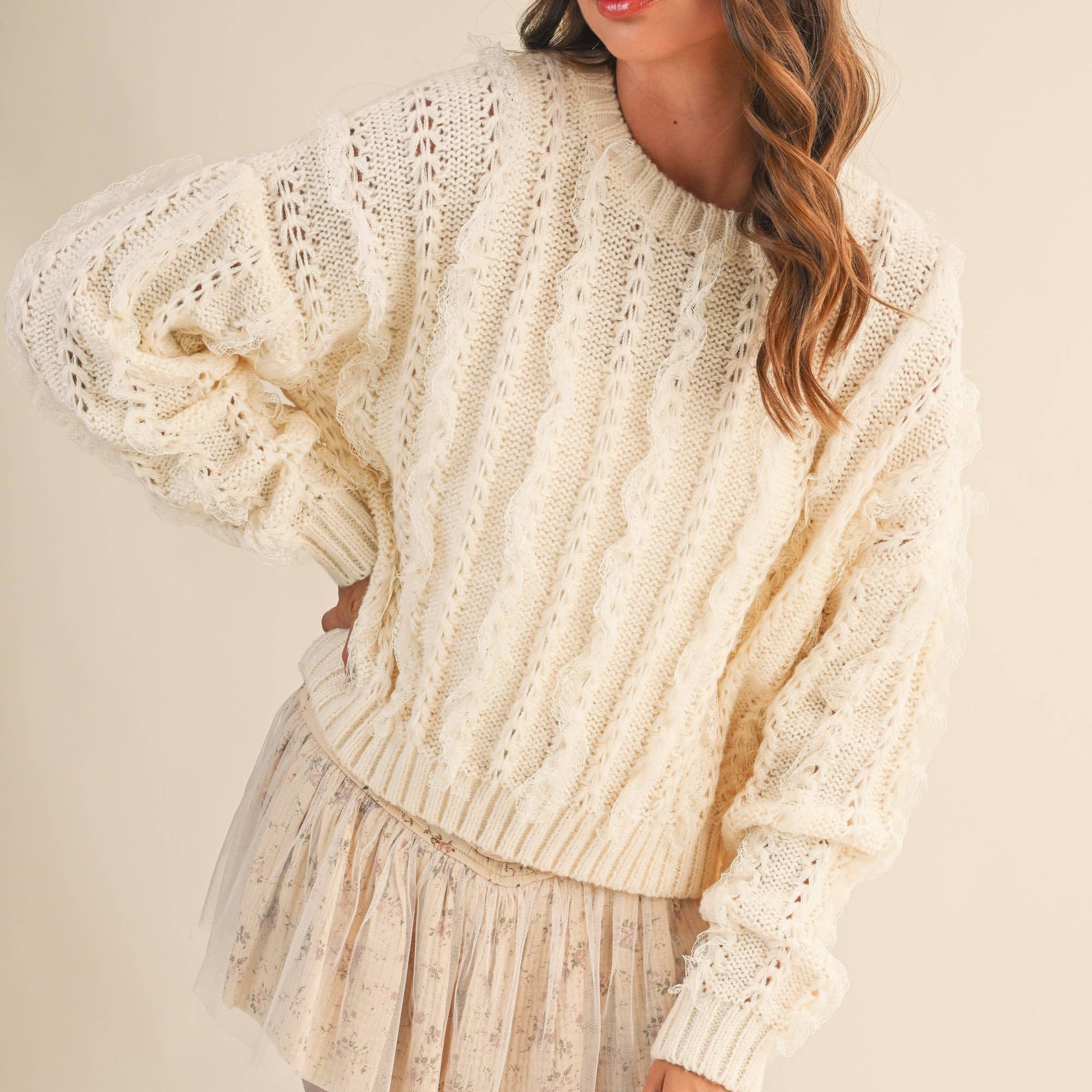 Woman wearing a cream-colored knit sweater and shorts on a plain background