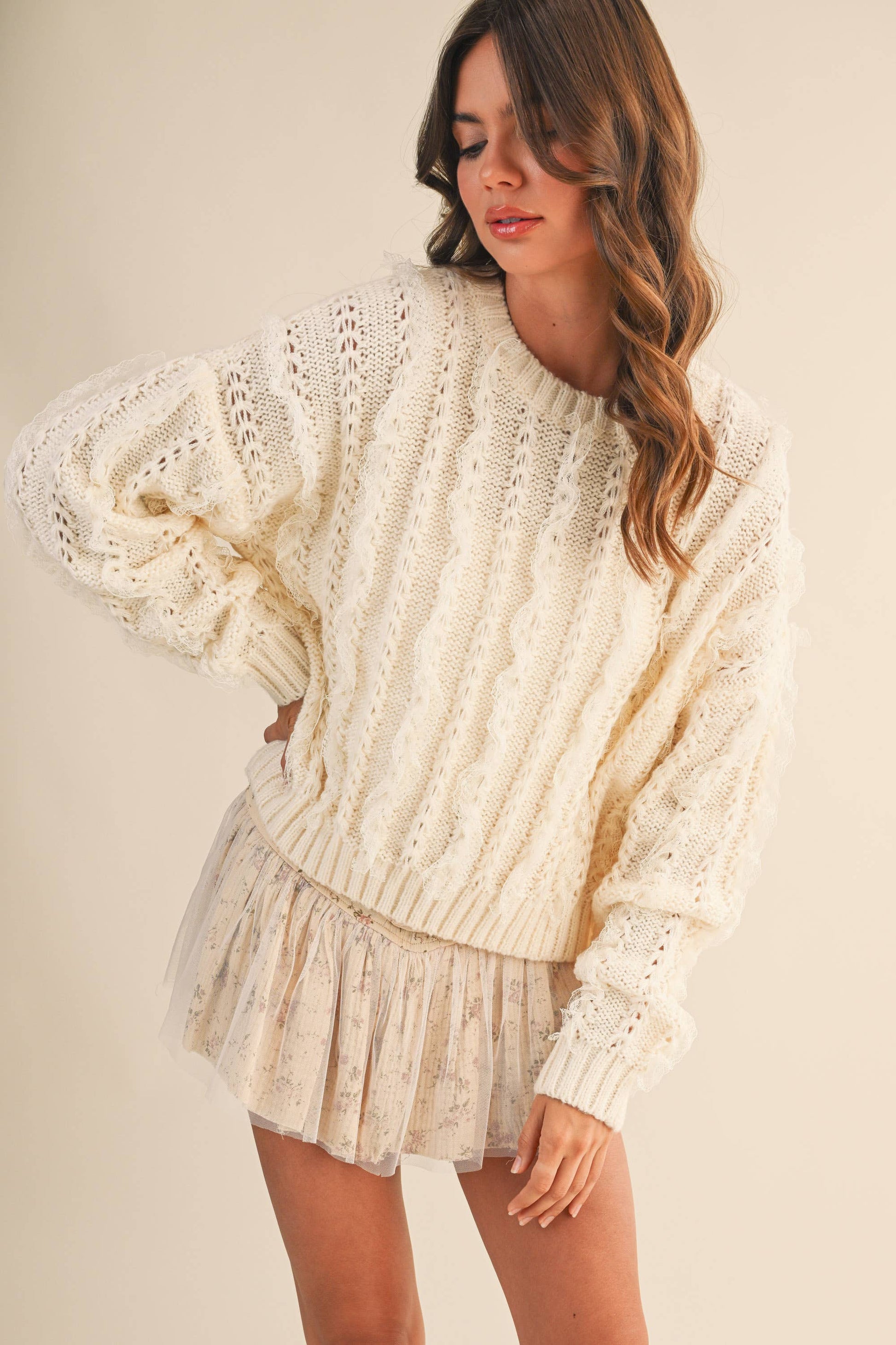 Woman wearing a cream-colored knit sweater and shorts on a plain background
