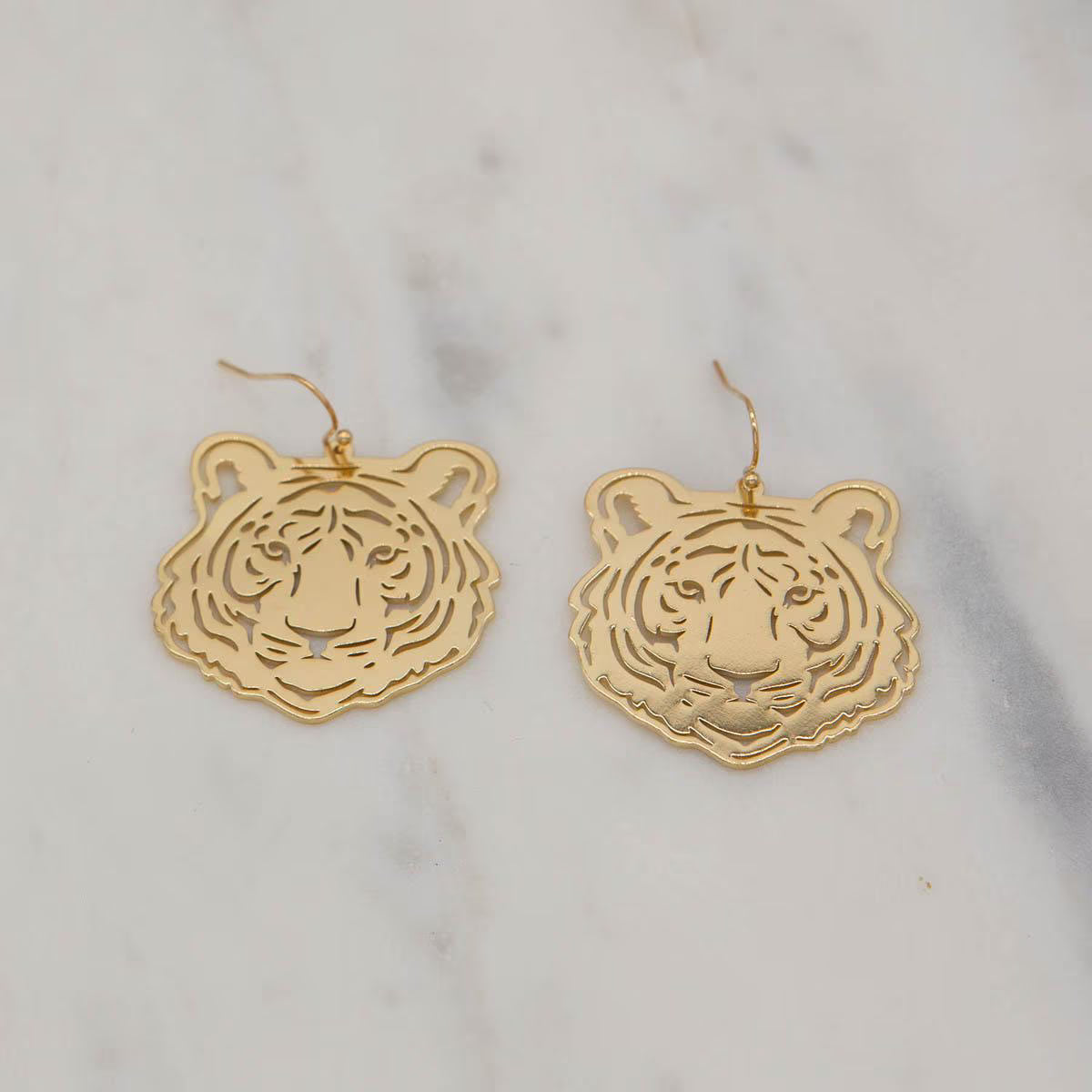 Gold tiger head earrings on a marble background