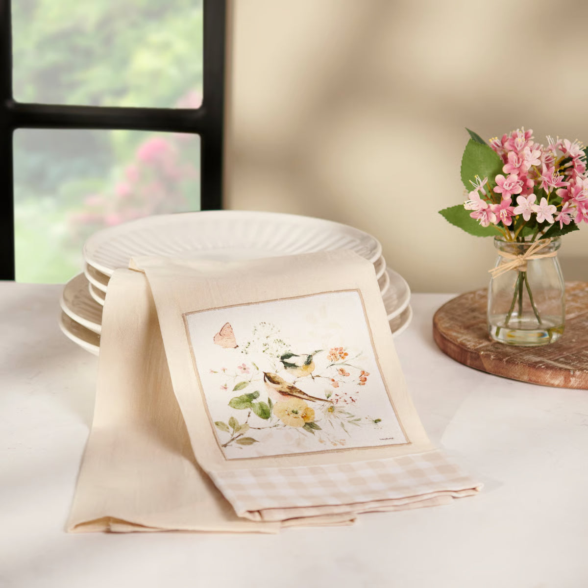 Decorative table setting with a folded napkin featuring a floral design, plates, and a vase with flowers.
