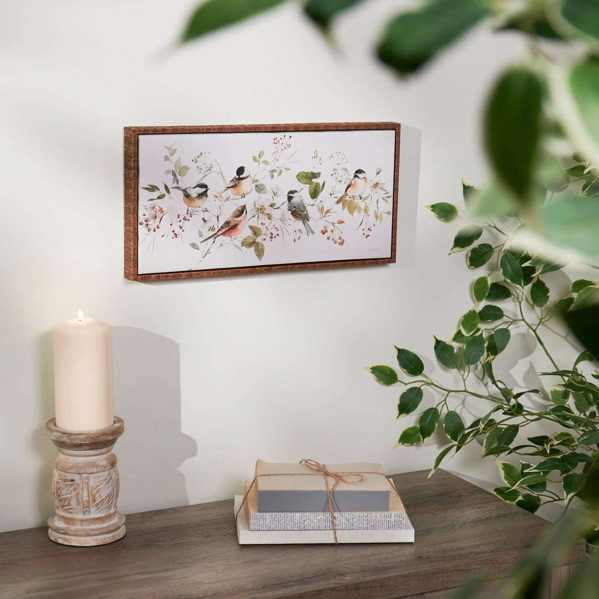 Decorative setup with a framed artwork of birds, candle, and books on a wooden surface.