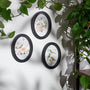 Three oval wall art pieces with floral and bird designs on a white wall, surrounded by green leaves.