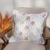A square throw pillow with a white background and a colorful geometric pattern, resting on a beige upholstered chair.