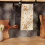 Floral-patterned towel hanging on a kitchen rack with wooden cutting board and utensils.