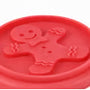 A close-up of a bright red silicone mold or stamp featuring a gingerbread man design, with a textured surface and a small circular hole near the top.