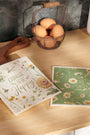 Two floral-themed greeting cards on a wooden surface with eggs and a basket in the background.