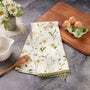 Floral-patterned towel on a kitchen counter with eggs, cutting board, and flowers.