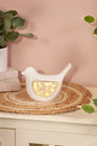 Decorative white bird-shaped lamp with gold内心 on a table with plants and books in the background.