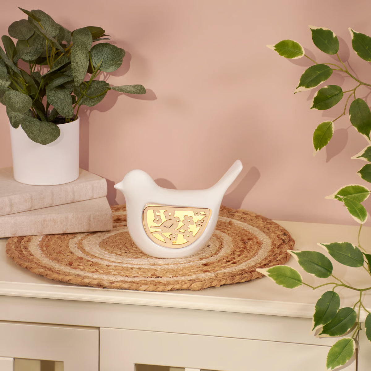 Decorative white bird-shaped lamp with gold内心 on a table with plants and books in the background.