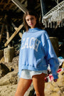 Woman wearing a blue 'BEACH' sweatshirt on a rocky beach.