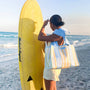 Woman holding a yellow surfboard on a beach with a clear sky