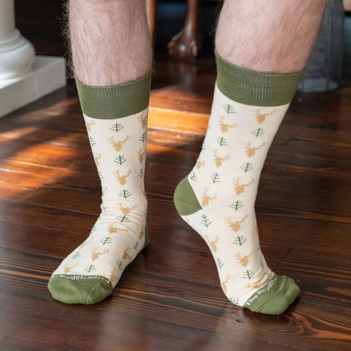 White socks with green tops and deer pattern worn by a person on a wooden floor.