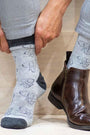 Person wearing gray socks with butterfly pattern and brown boots on a neutral background