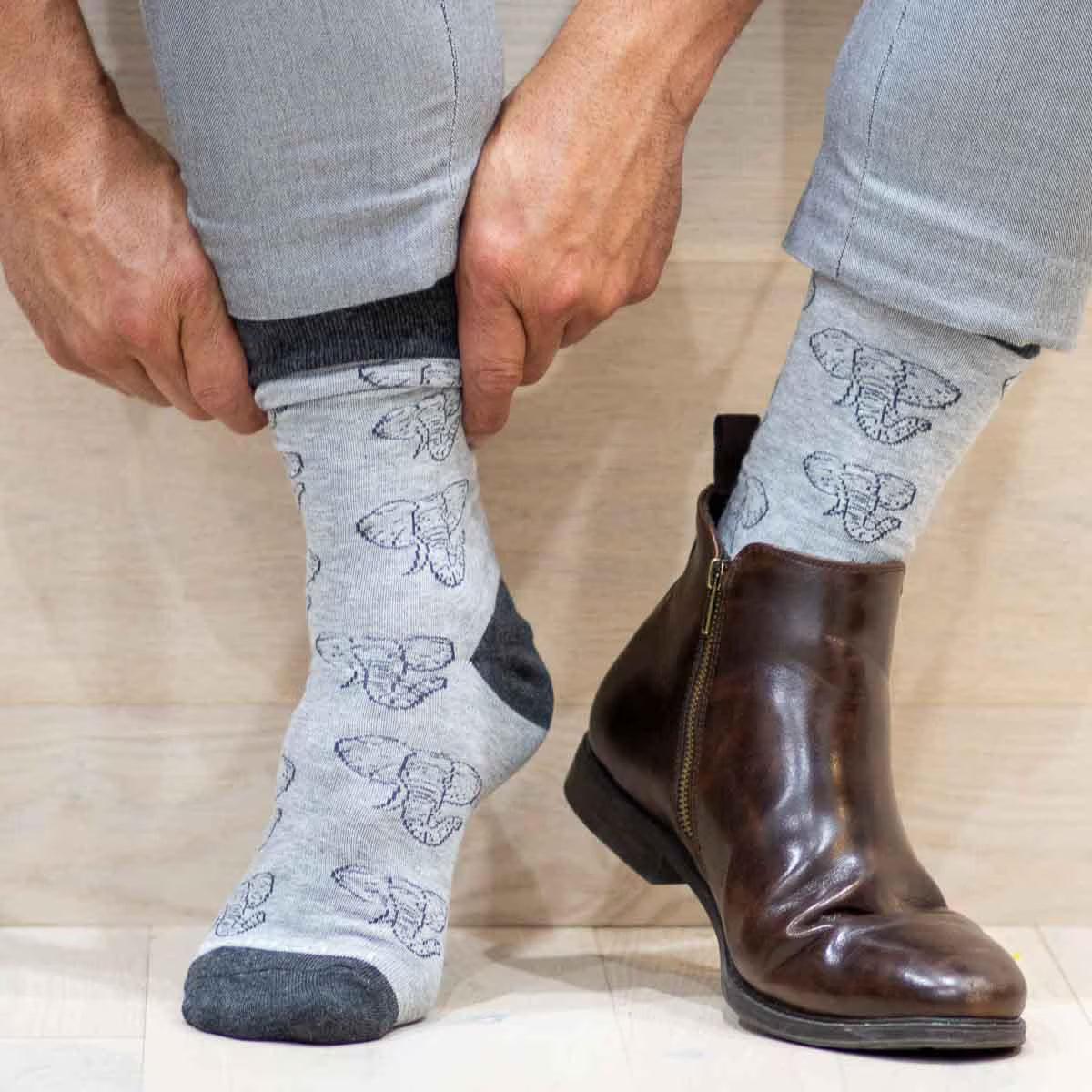 Person wearing gray socks with butterfly pattern and brown boots on a neutral background