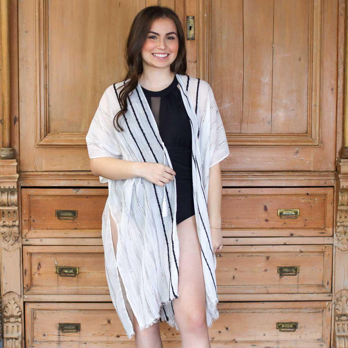 Woman wearing a white and black striped cover-up in front of wooden furniture.