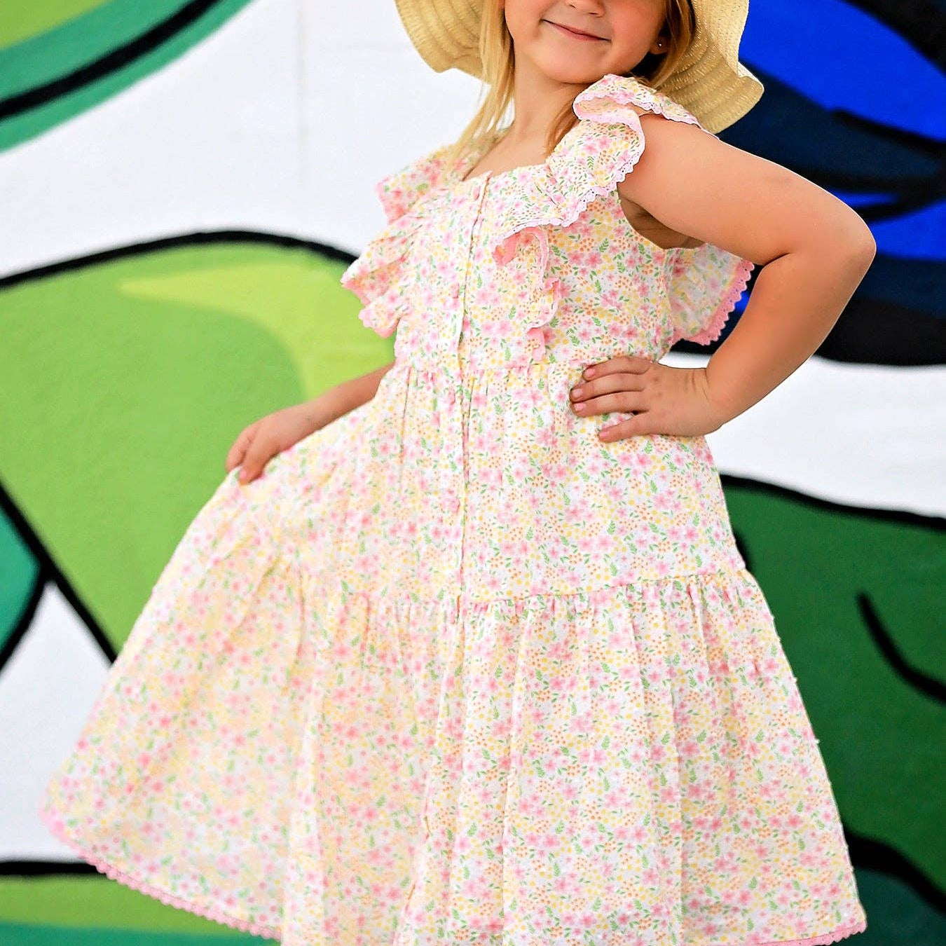 Young girl in a floral dress and sun hat posing in front of a colorful abstract background