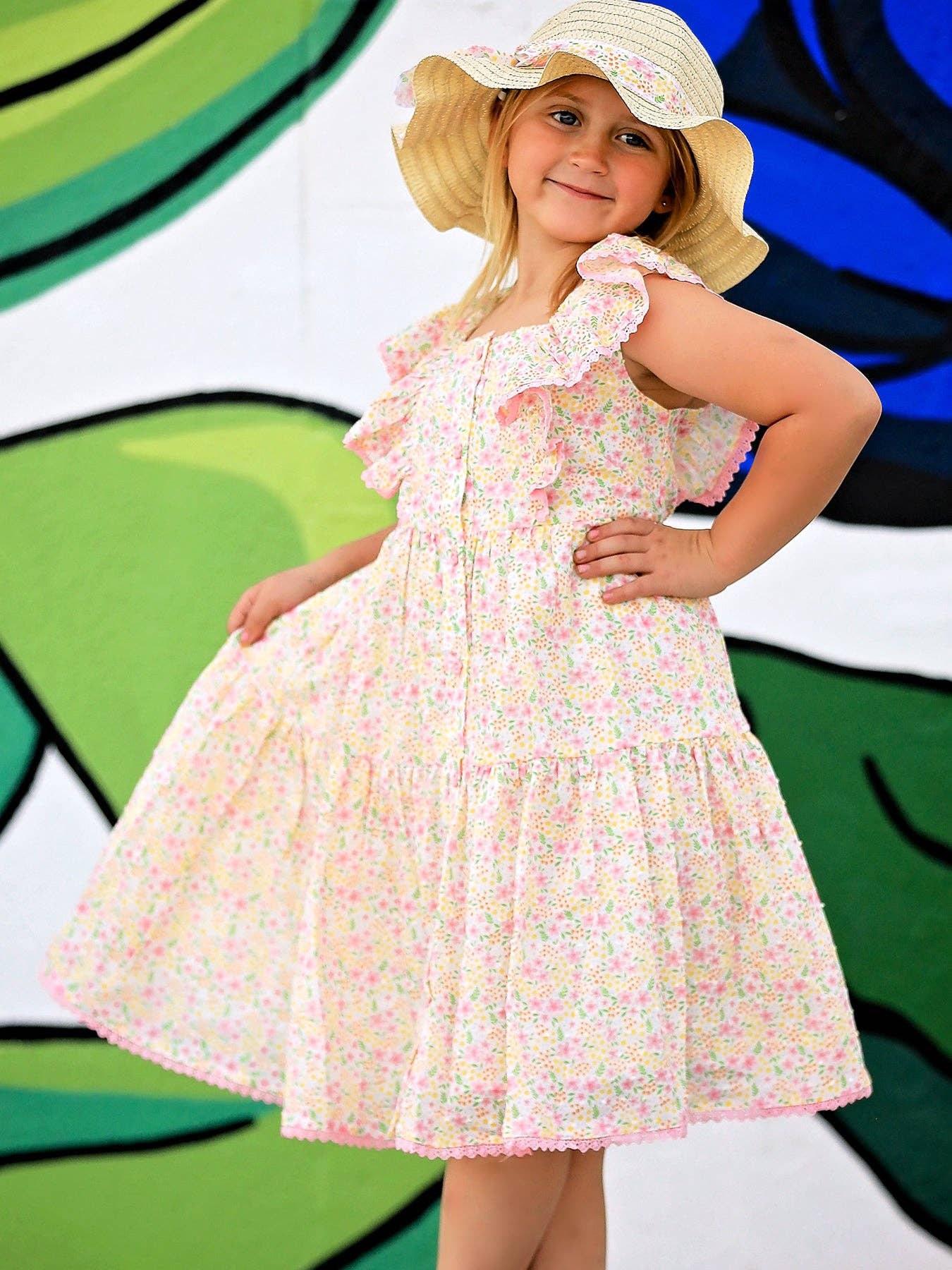 Young girl in a floral dress and sun hat posing in front of a colorful abstract background