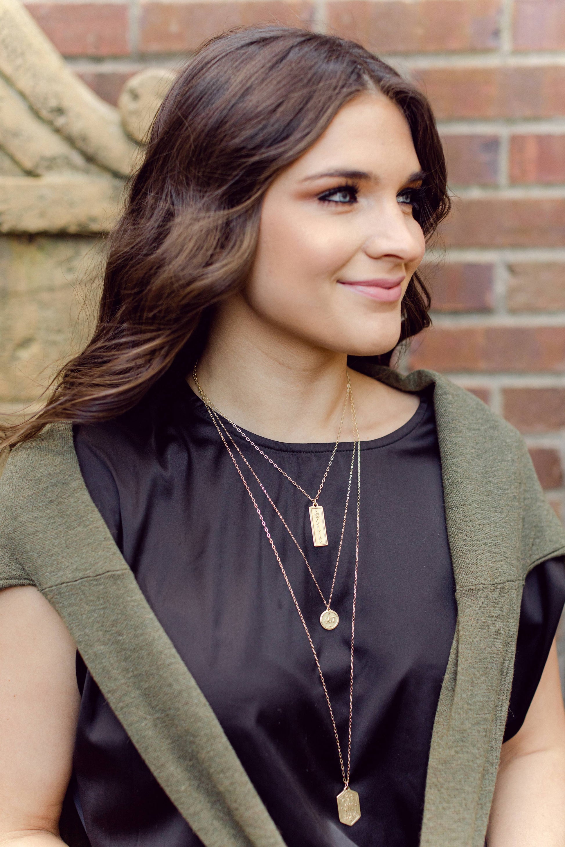 Woman wearing layered necklaces in front of a brick wall