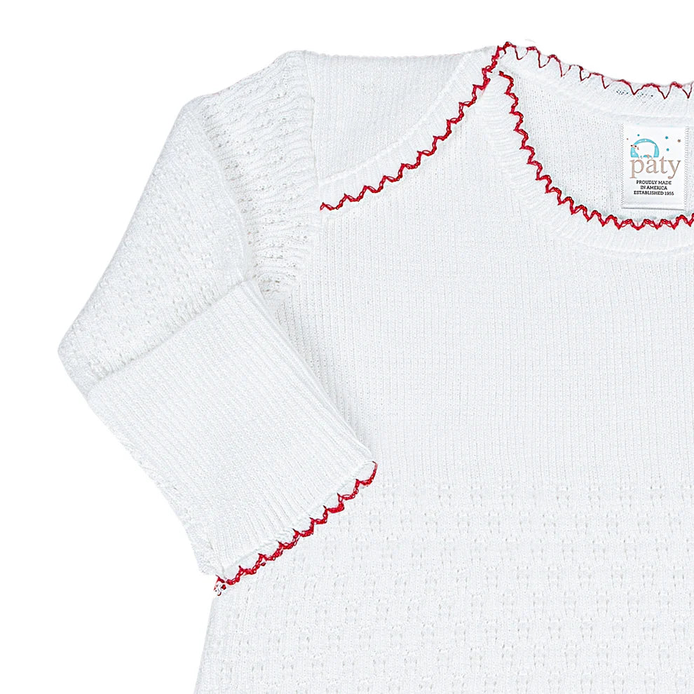 White baby gown with red trim on a white background