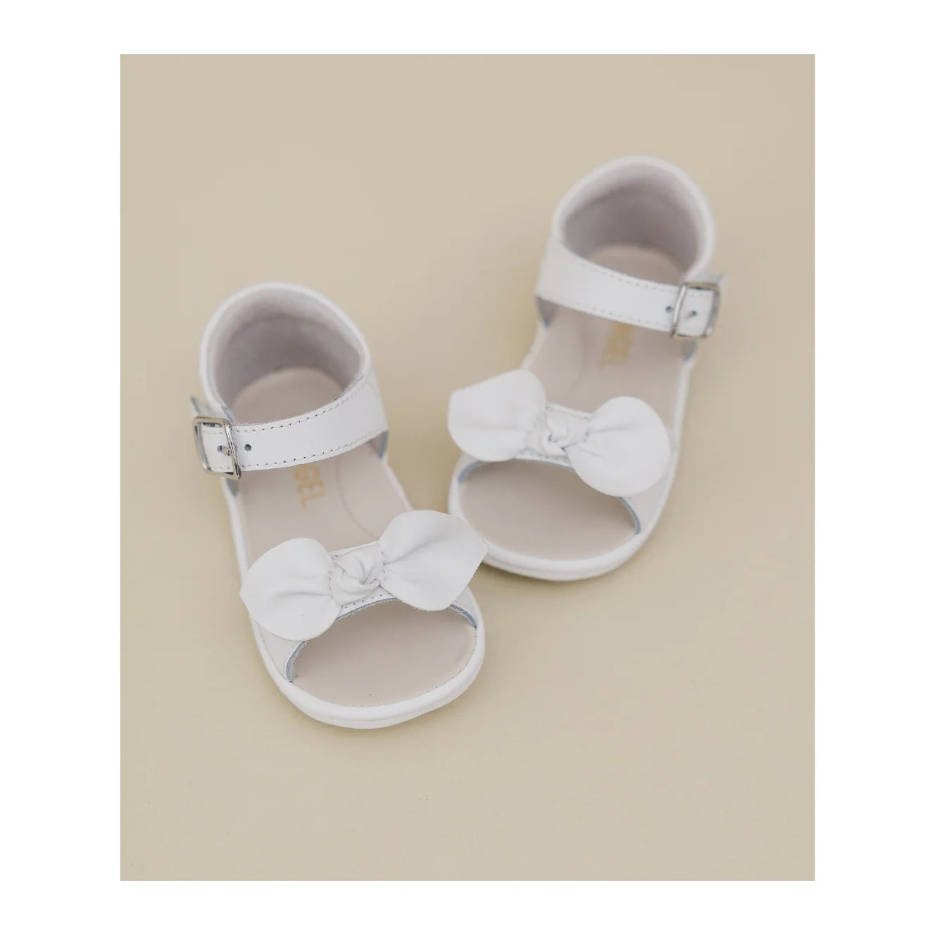 White baby sandals with bow details on a beige background
