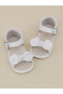White baby sandals with bow details on a beige background