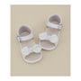 White baby sandals with bow details on a beige background